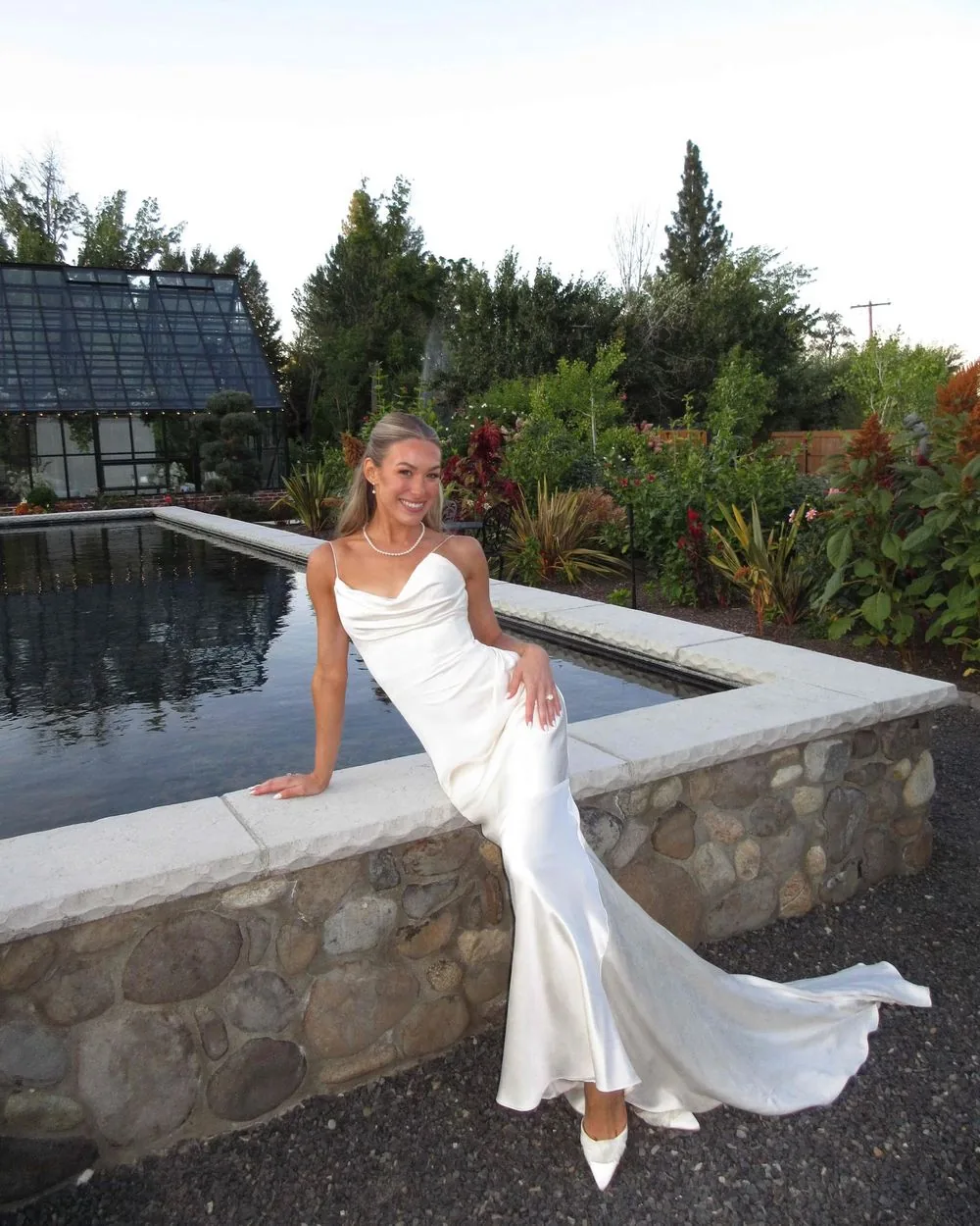Bride in a silk slip dress sitting on the edge of a garden pond