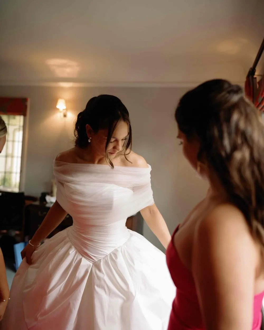 Bride getting ready in an off the shoulder gown with her bridesmaid